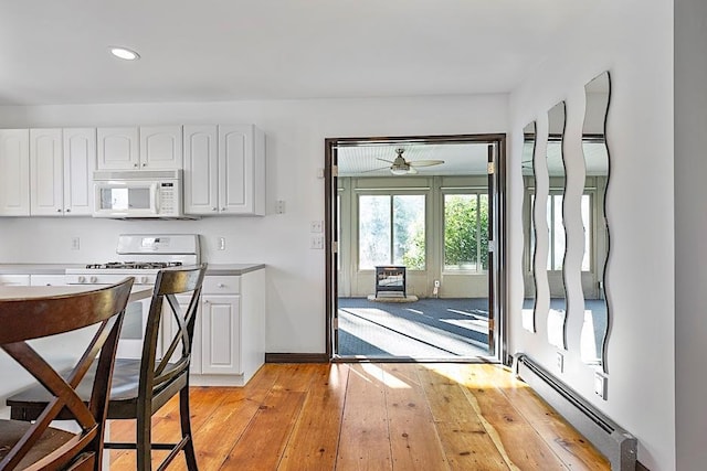 kitchen featuring white cabinetry, white appliances, ceiling fan, light wood-type flooring, and a baseboard radiator