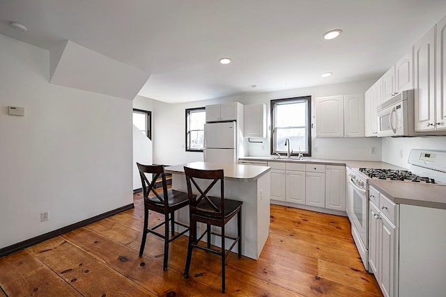 kitchen featuring white appliances, white cabinetry, a center island, and light wood-type flooring