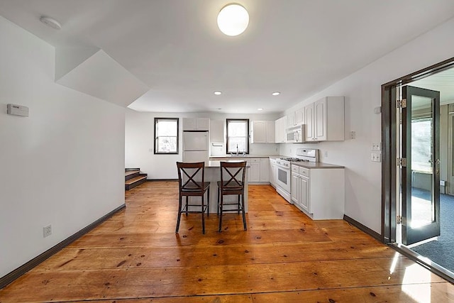 kitchen with white cabinetry, white appliances, light wood-type flooring, a kitchen island, and a breakfast bar