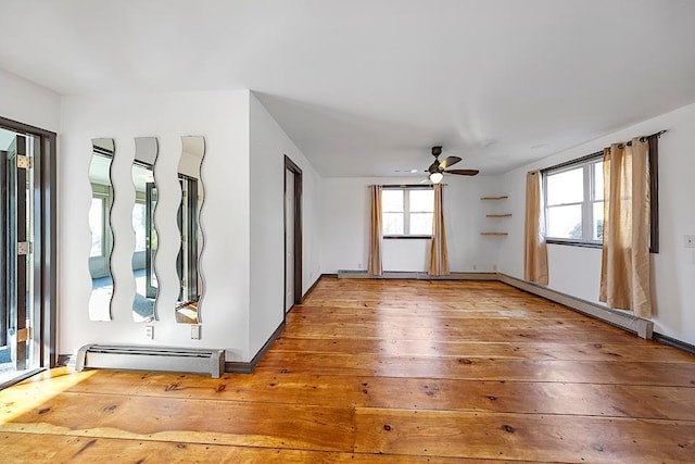 empty room featuring ceiling fan, baseboard heating, a wealth of natural light, and hardwood / wood-style flooring