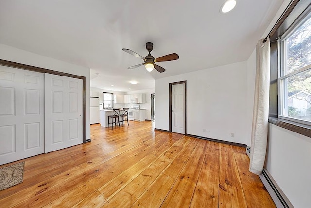 unfurnished bedroom with light hardwood / wood-style floors, multiple windows, baseboard heating, and white fridge