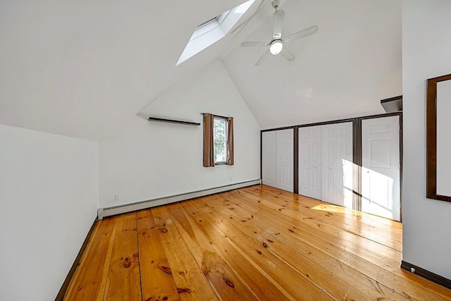 additional living space featuring a baseboard heating unit, ceiling fan, vaulted ceiling with skylight, and wood-type flooring