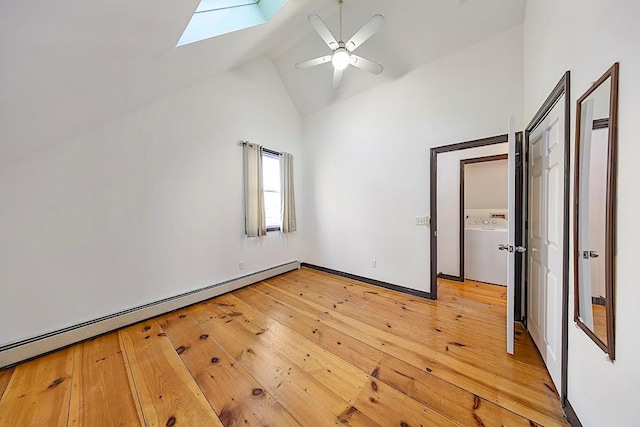 unfurnished bedroom featuring light wood-type flooring, ceiling fan, washer / dryer, vaulted ceiling with skylight, and a baseboard heating unit