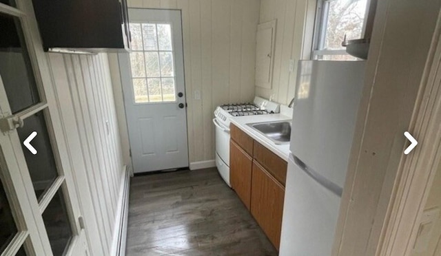 kitchen featuring dark hardwood / wood-style floors, wood walls, white appliances, and sink