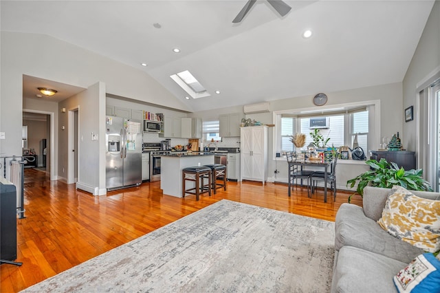 living room with light hardwood / wood-style floors, lofted ceiling with skylight, ceiling fan, and an AC wall unit