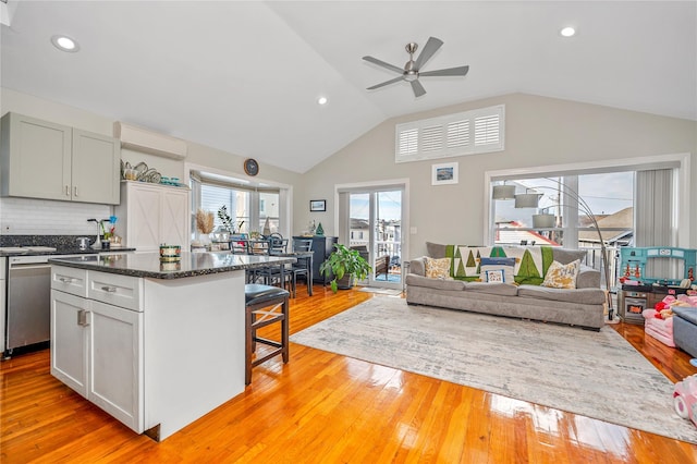 kitchen featuring tasteful backsplash, stainless steel dishwasher, a wall unit AC, a kitchen bar, and light wood-type flooring