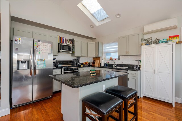 kitchen with vaulted ceiling with skylight, stainless steel appliances, an AC wall unit, a kitchen island, and a breakfast bar area