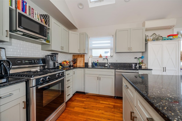 kitchen with an AC wall unit, sink, vaulted ceiling, hardwood / wood-style flooring, and appliances with stainless steel finishes