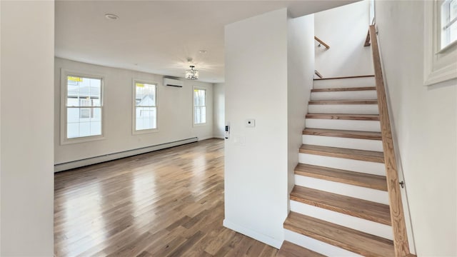 stairs with hardwood / wood-style flooring, a wall unit AC, plenty of natural light, and a baseboard heating unit