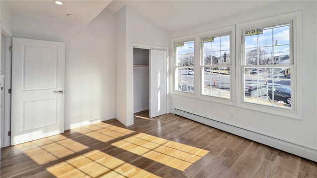 unfurnished bedroom featuring multiple windows, a closet, vaulted ceiling, and a baseboard heating unit