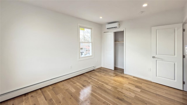 unfurnished bedroom featuring baseboard heating, a closet, light hardwood / wood-style floors, and a wall mounted air conditioner