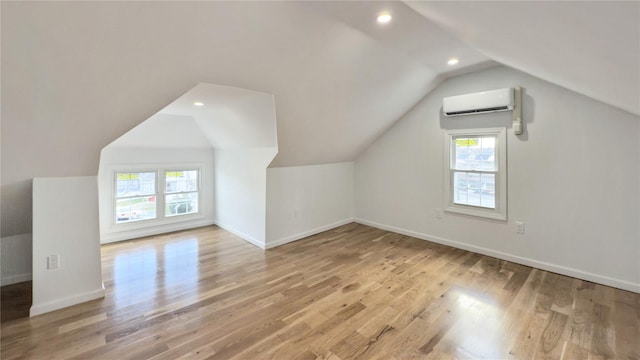 bonus room with light wood-type flooring, vaulted ceiling, an AC wall unit, and a healthy amount of sunlight