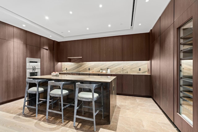 kitchen with stainless steel double oven, light countertops, a center island, modern cabinets, and a kitchen bar