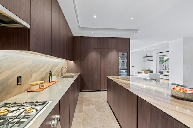 kitchen with stainless steel gas cooktop, a sink, light countertops, dark brown cabinets, and modern cabinets