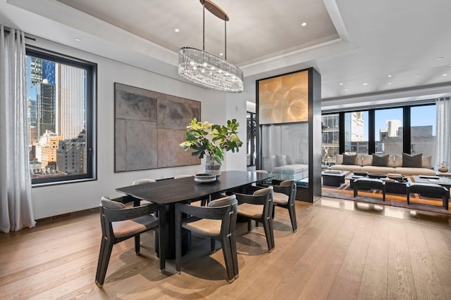 dining space with a city view, a raised ceiling, light wood-style flooring, and a healthy amount of sunlight