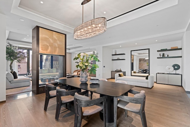 dining area with light wood-type flooring, a tray ceiling, a chandelier, and recessed lighting