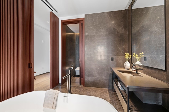 bathroom with visible vents, toilet, a freestanding bath, vanity, and tile walls