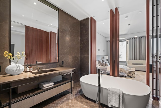 ensuite bathroom with brick floor, a notable chandelier, tile walls, a soaking tub, and vanity