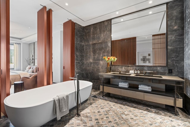 full bath featuring double vanity, a soaking tub, a sink, and tile walls