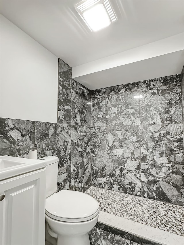 bathroom with vanity, tiled shower, tile walls, and toilet