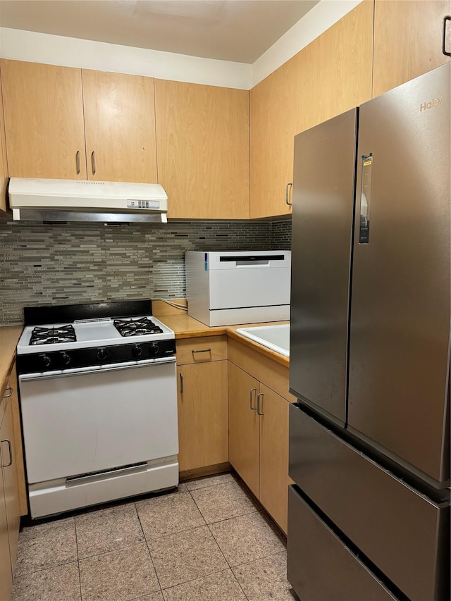 kitchen featuring white range with gas stovetop, stainless steel fridge, light brown cabinets, and tasteful backsplash