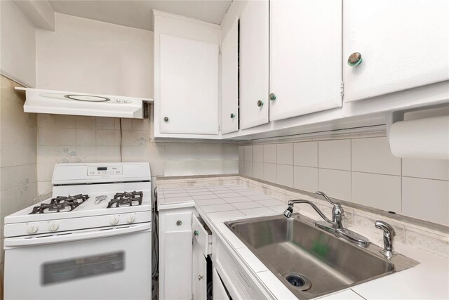 kitchen with white gas range oven, backsplash, ventilation hood, sink, and white cabinets