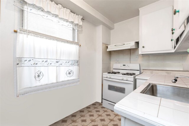 kitchen with tile counters, white cabinetry, white range with gas stovetop, and extractor fan