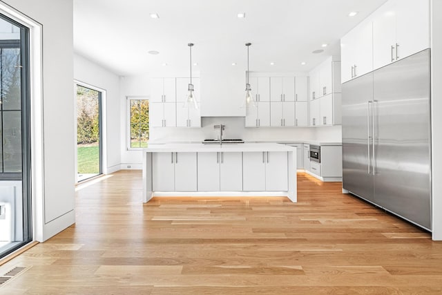 kitchen with built in fridge, white cabinets, light wood-type flooring, and hanging light fixtures