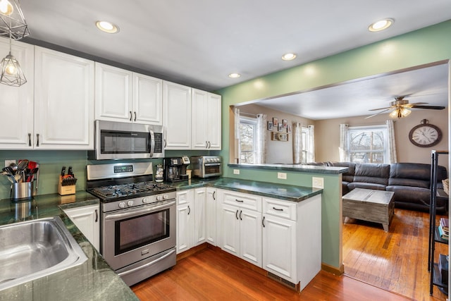 kitchen featuring white cabinetry, stainless steel appliances, dark hardwood / wood-style floors, kitchen peninsula, and pendant lighting