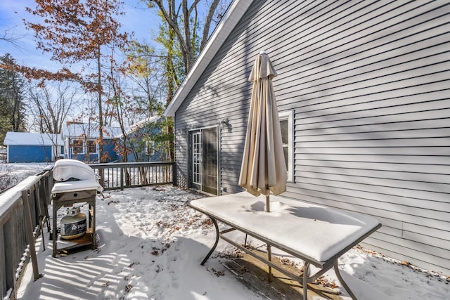 snow covered patio with area for grilling and a wooden deck