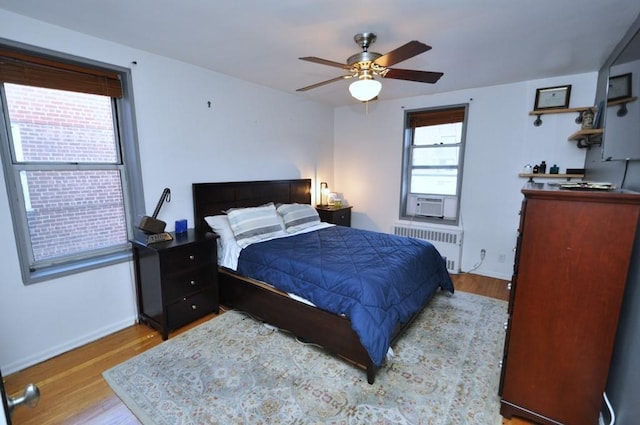 bedroom featuring ceiling fan, light wood-type flooring, radiator, and multiple windows