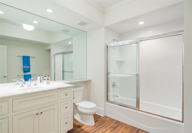 full bathroom featuring crown molding, hardwood / wood-style floors, toilet, shower / bath combination with glass door, and vanity