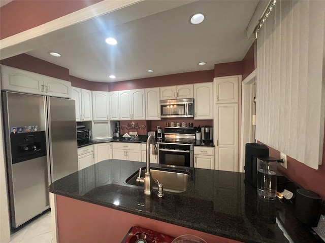 kitchen with dark stone counters, sink, light tile patterned floors, appliances with stainless steel finishes, and white cabinetry