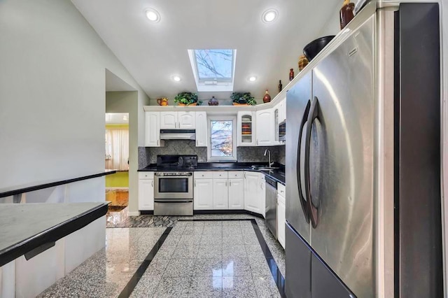 kitchen with decorative backsplash, appliances with stainless steel finishes, a skylight, sink, and white cabinetry