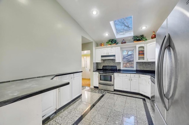 kitchen featuring decorative backsplash, a skylight, stainless steel appliances, high vaulted ceiling, and white cabinets