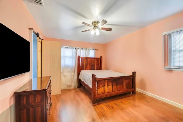 bedroom with a barn door, ceiling fan, and light hardwood / wood-style floors