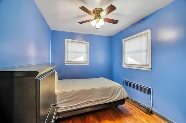 unfurnished bedroom with ceiling fan, wood-type flooring, and radiator heating unit