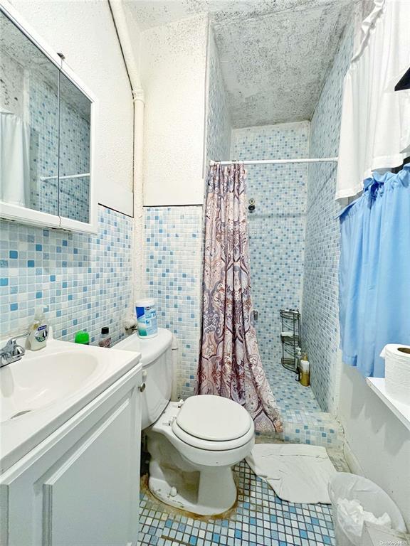 bathroom featuring a shower with shower curtain, vanity, toilet, and tile walls