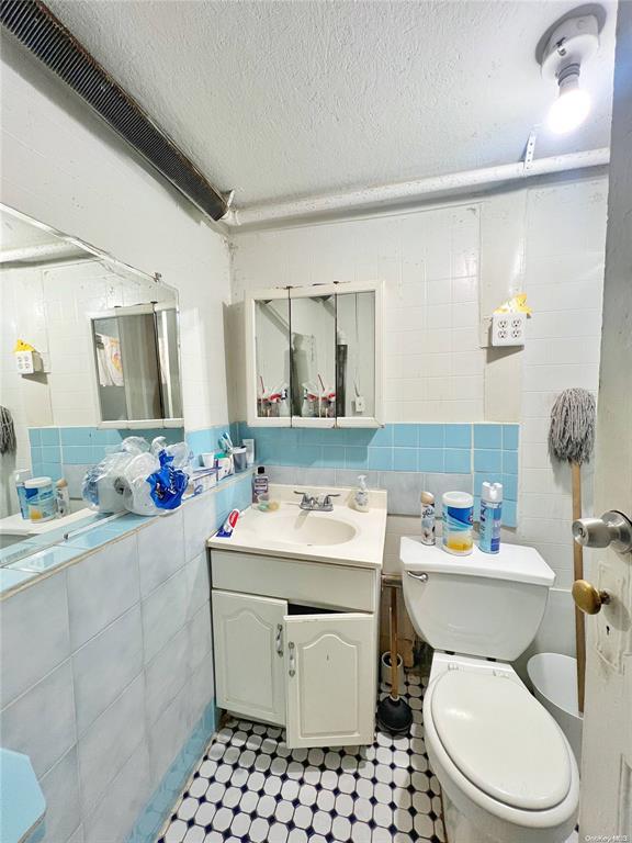 bathroom featuring vanity, decorative backsplash, toilet, a textured ceiling, and tile walls