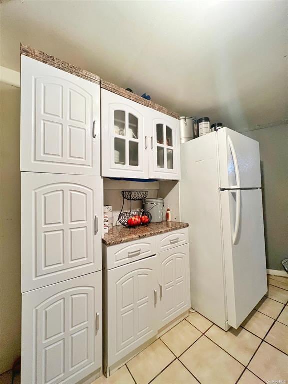 kitchen with light tile patterned floors, white fridge, white cabinetry, and dark stone counters