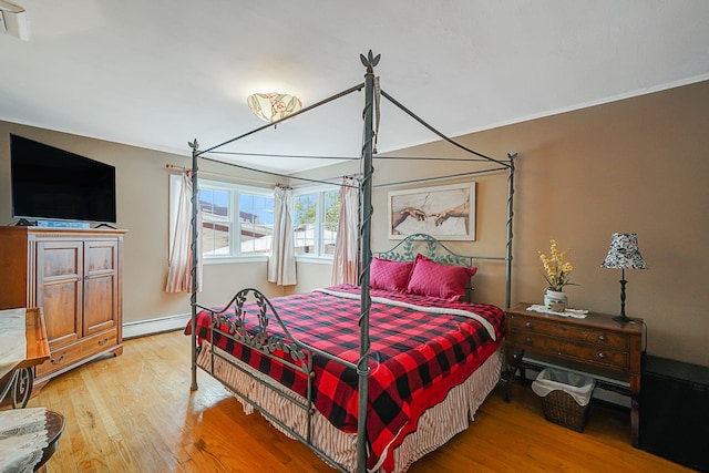 bedroom featuring ornamental molding, baseboard heating, and light hardwood / wood-style flooring