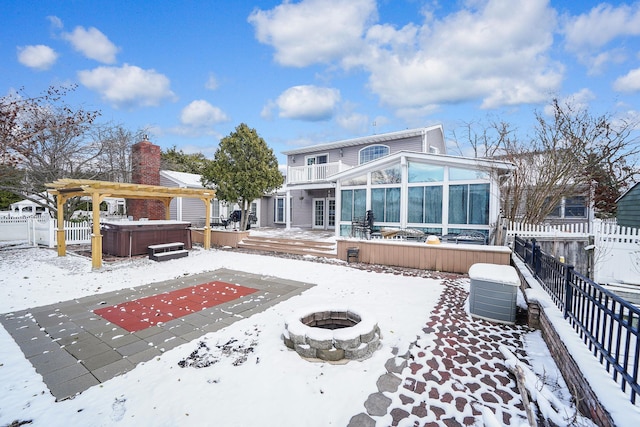 snow covered property with a sunroom, a deck, an outdoor fire pit, and a hot tub