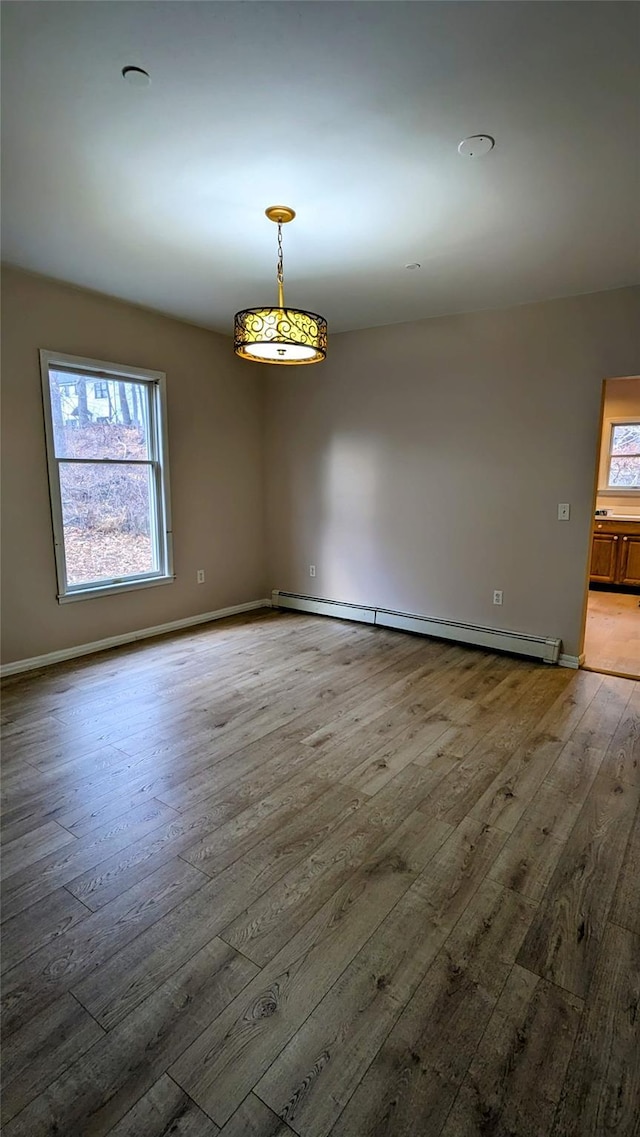 empty room featuring hardwood / wood-style flooring, a wealth of natural light, and a baseboard radiator