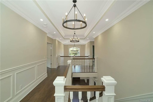 stairway with a notable chandelier, a raised ceiling, a decorative wall, and wood finished floors