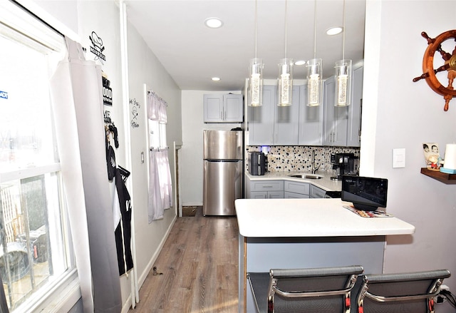 kitchen featuring kitchen peninsula, stainless steel fridge, pendant lighting, a kitchen bar, and gray cabinets