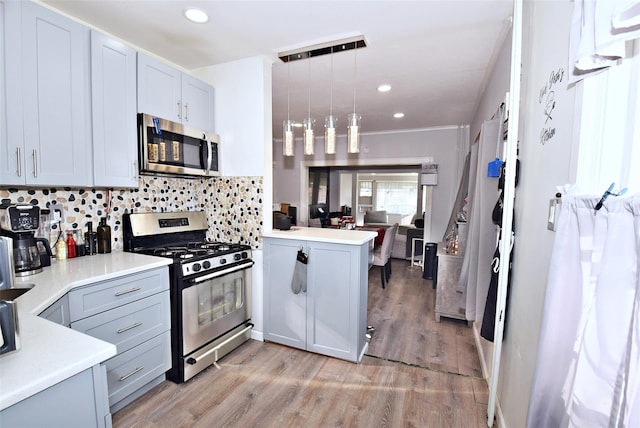 kitchen featuring backsplash, kitchen peninsula, light hardwood / wood-style floors, pendant lighting, and appliances with stainless steel finishes