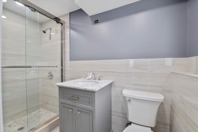 bathroom with a shower with door, vanity, tile walls, and toilet