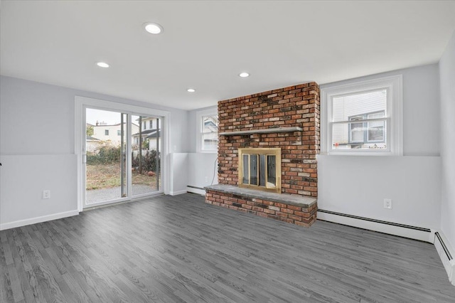 unfurnished living room featuring a brick fireplace, dark wood-type flooring, a wealth of natural light, and a baseboard radiator