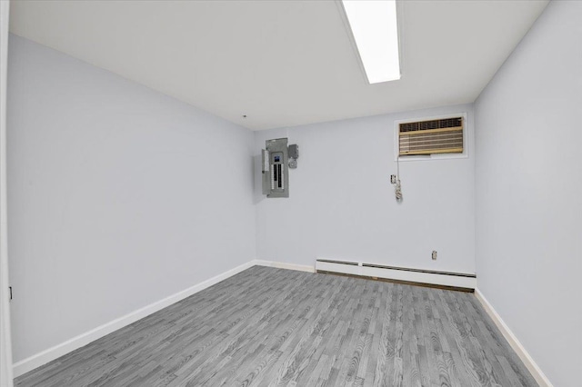 unfurnished room featuring electric panel, hardwood / wood-style flooring, an AC wall unit, and baseboard heating