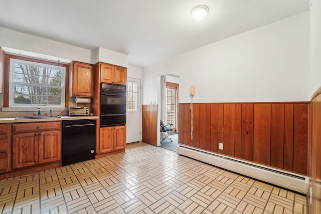 kitchen with sink, black dishwasher, wooden walls, and a baseboard heating unit